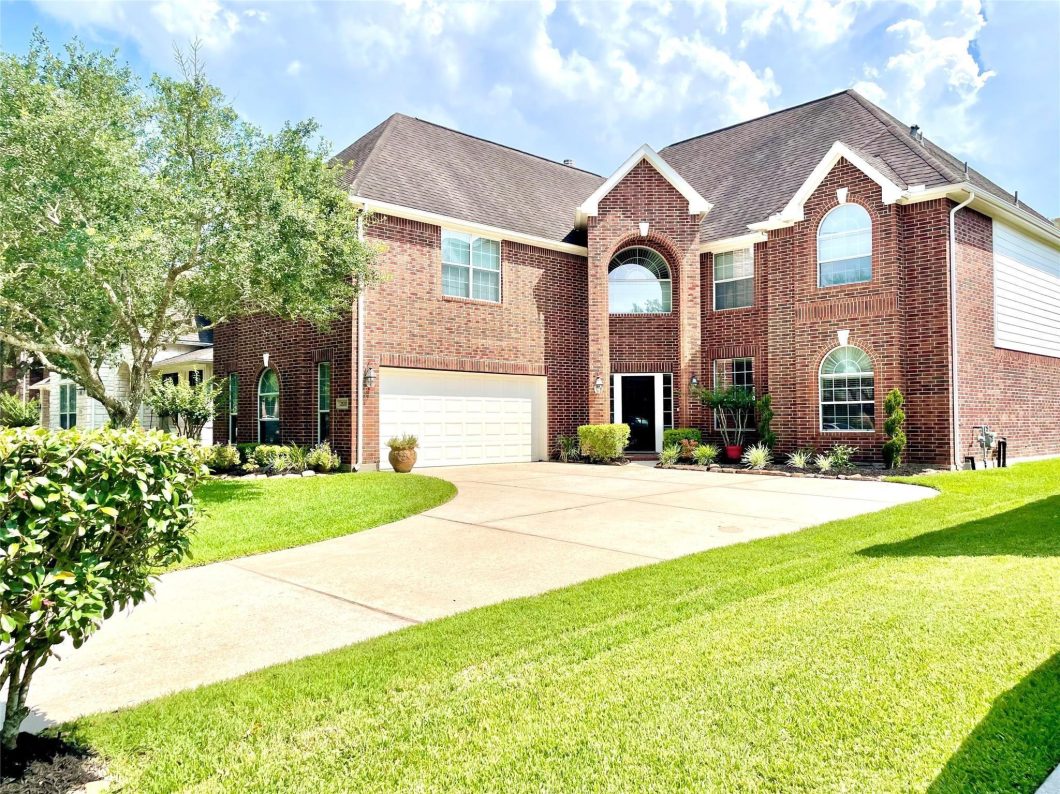 Immaculate brick home in Friendswood with manicured lawn, featuring a two-car garage, large windows, and elegant architectural details, ideal for families seeking residential lease options.
